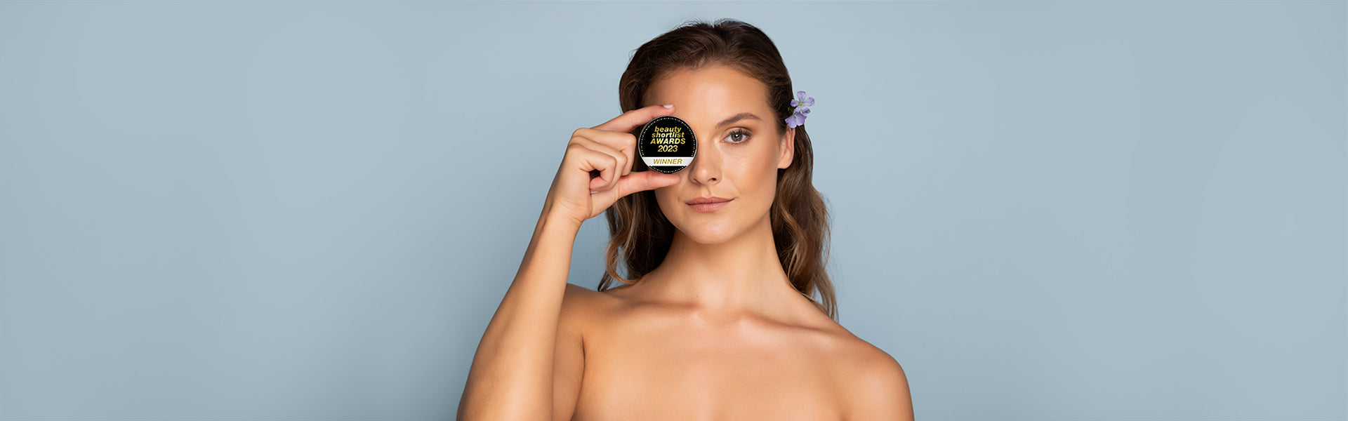 Woman holds beauty shortlist award badge up to her eye